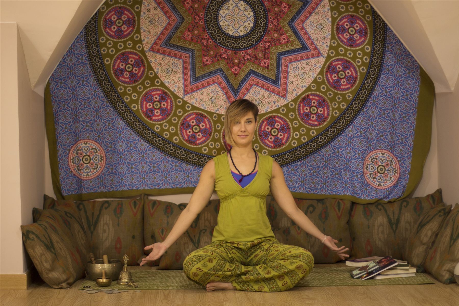 Retrato de Gema Núñez sentada en postura de meditación ante un gran mandala, con las palmas abiertas y un cuenco tibetano a su lado.